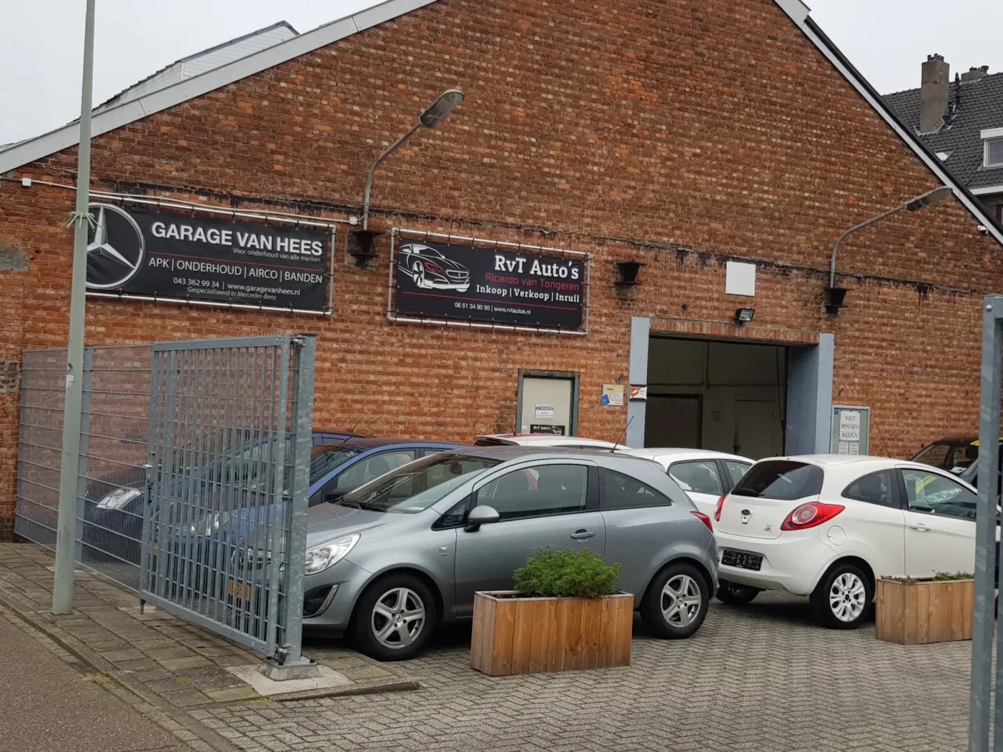 De gevel van Garage van Hees met het naambord, het hek en auto's op het terrein