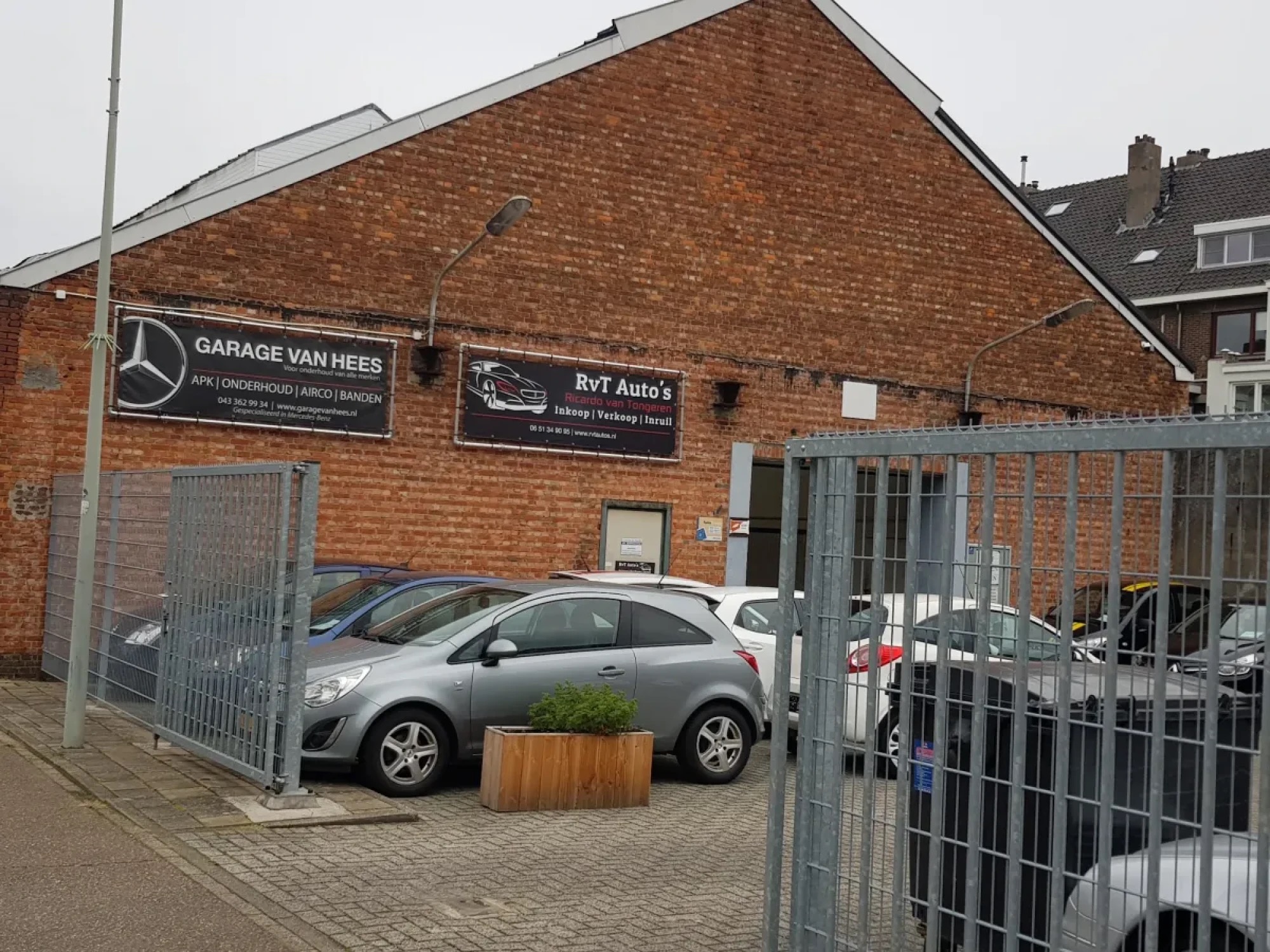De bakstenen gevel van Garage van Hees gezien door het hek, met een bloembak op het terrein