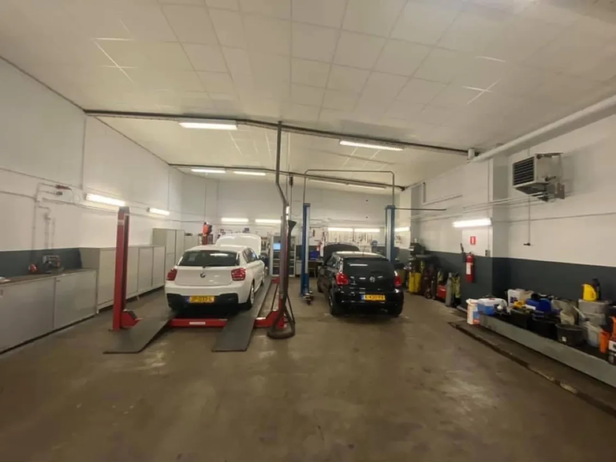 De werkplaats van binnen, met twee bruggen waarop een witte BMW en een zwarte Volkswagen staan